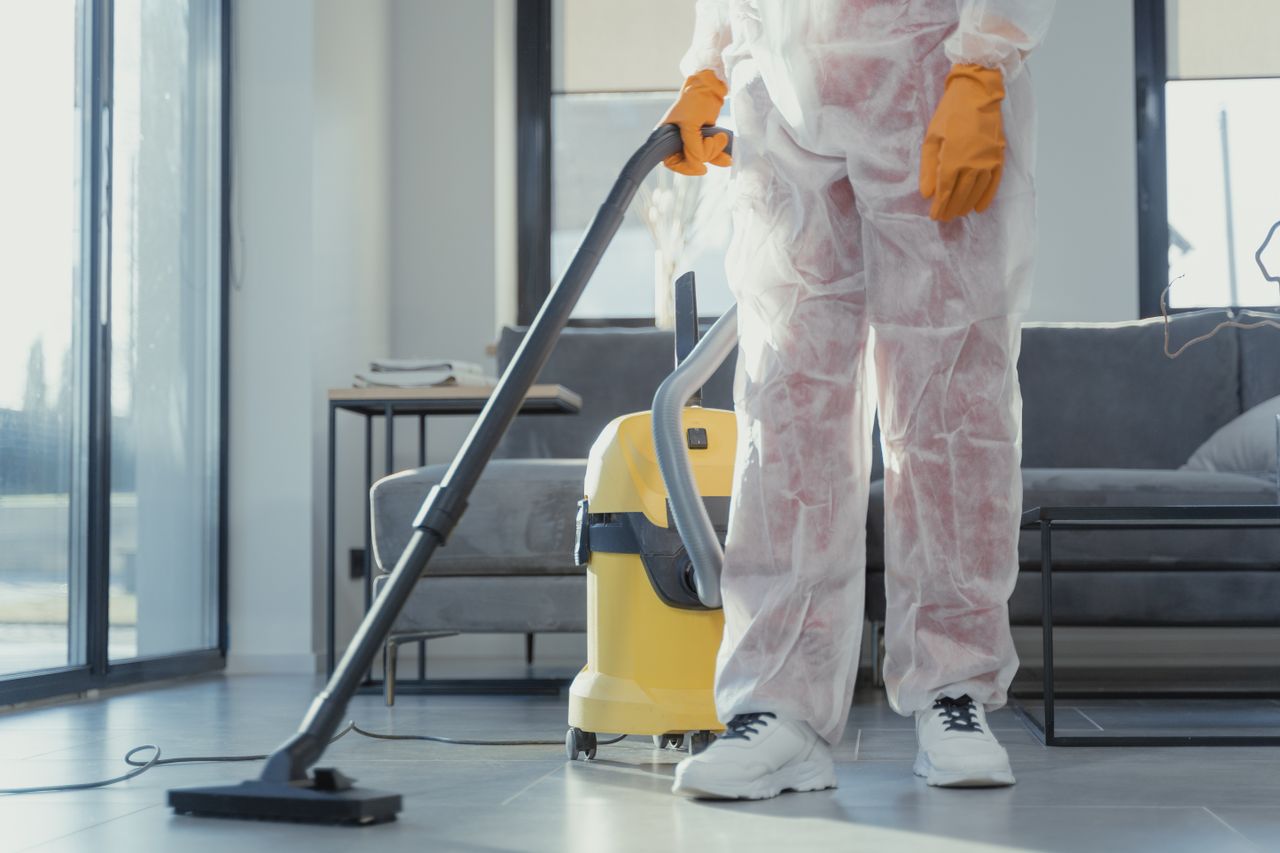 hero-img A cleaner in protective coveralls and gloves vacuuming a modern living room.